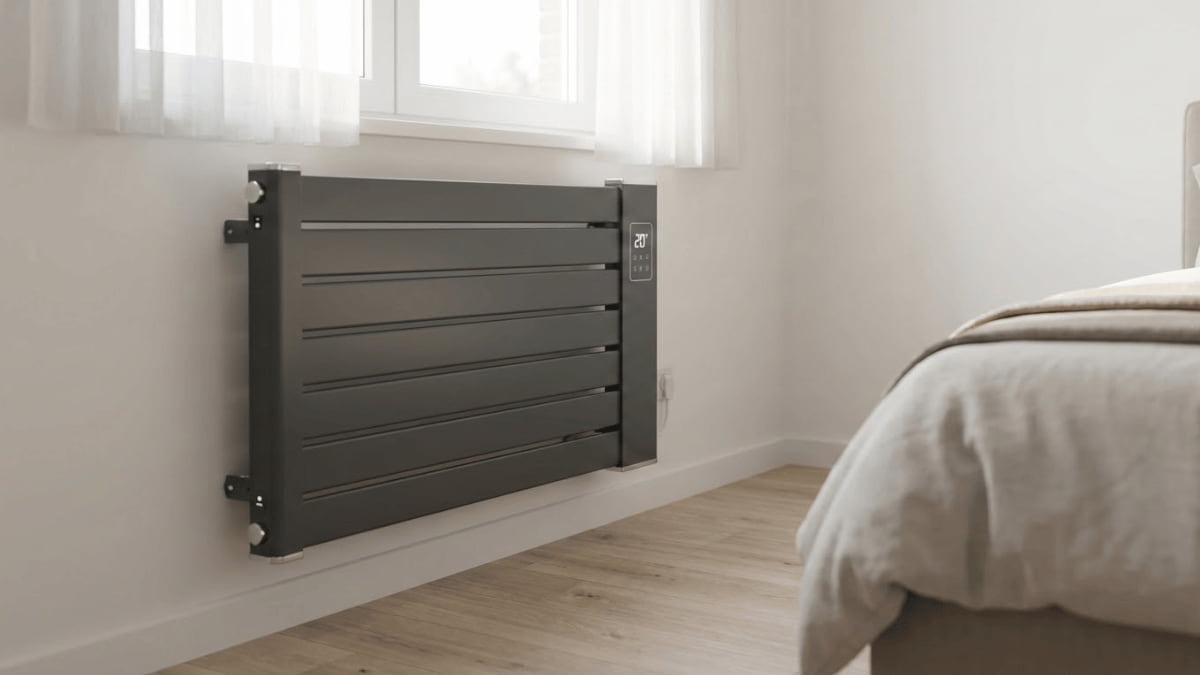 Elektrische radiator gemonteerd aan de muur in een moderne slaapkamer, met een strak design, houten vloer en daglicht via het raam.